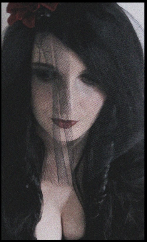 jennydreiSchleierRose Portrait einer Frau mit schwarzen Haaren, schwarzer Bluse, schwarzem durchsichtigen Schleier und schwarz geschminkten Augen..