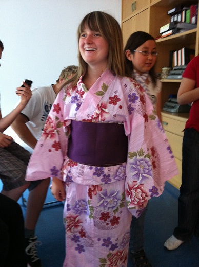 Eine lachende Frau im rosa Kimono, um die mehrere Leute herumlaufen.