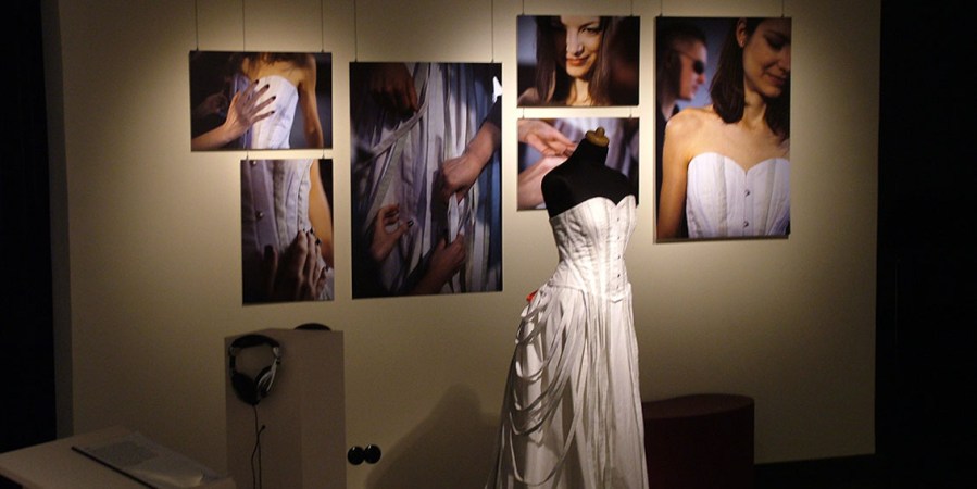 Kleiderpuppe mit langem schwarz-weißen Kleid. Im Hintergrund großformatige Fotos der Ausstellung