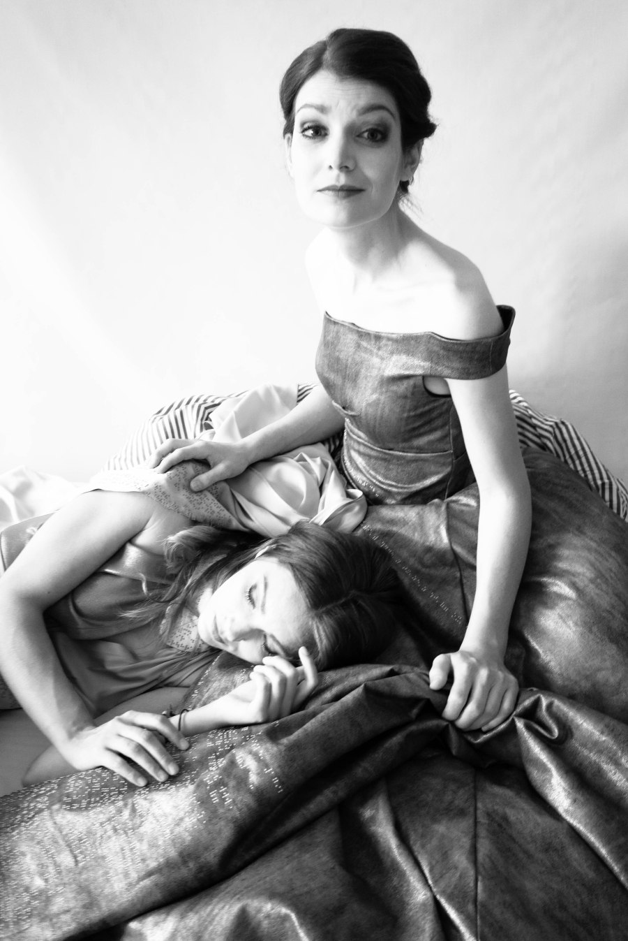 Eine junge, lanhaarige Frau liegt mit dem Kopf im Schoß einer jungen, kurzhaarigen Frau in einem trägerlosen Kleid. Schwarz-Weiß