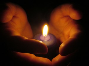 Zwei Hände, die eine Kerzenflamme umfassen, nur von dieser beleuchtet