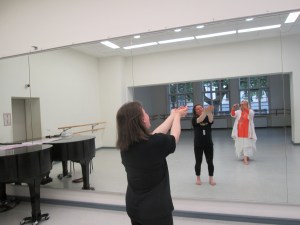 Eine Frau, die eine Tanzbewegung macht, vor einem Spiegel, in dem man auch die Fotografin dieses Bildes spiegelt.