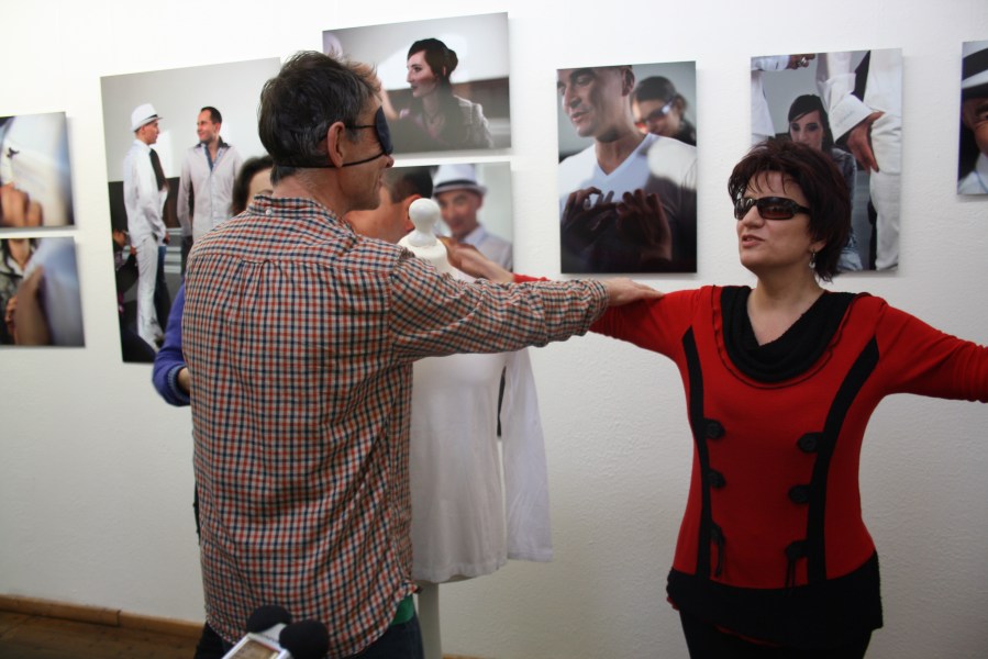 Ein Mann mit verbundenen Augen betastet die Frau im roten Pullover