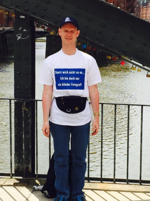 Christian mit einem T-Shirt auf dem steht: Starrt mich nicht so an ... Ich bin doch bloß ein blinder Fotograf.