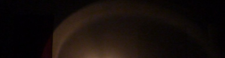 Schwarzer Hintergrund in dessen unterer Hälfte eine Person von einer Lichtquelle angestrahlt wird