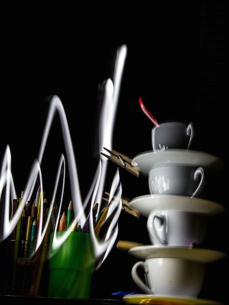 Gestapelte Tassen und aufrecht stehendes Besteck vor schwarzem Hintergrund