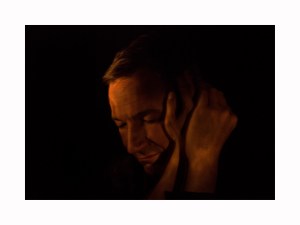 Ein geneigter Kopf mit geschlossenen Augen, seitlich zwei Hände ihn berührend.